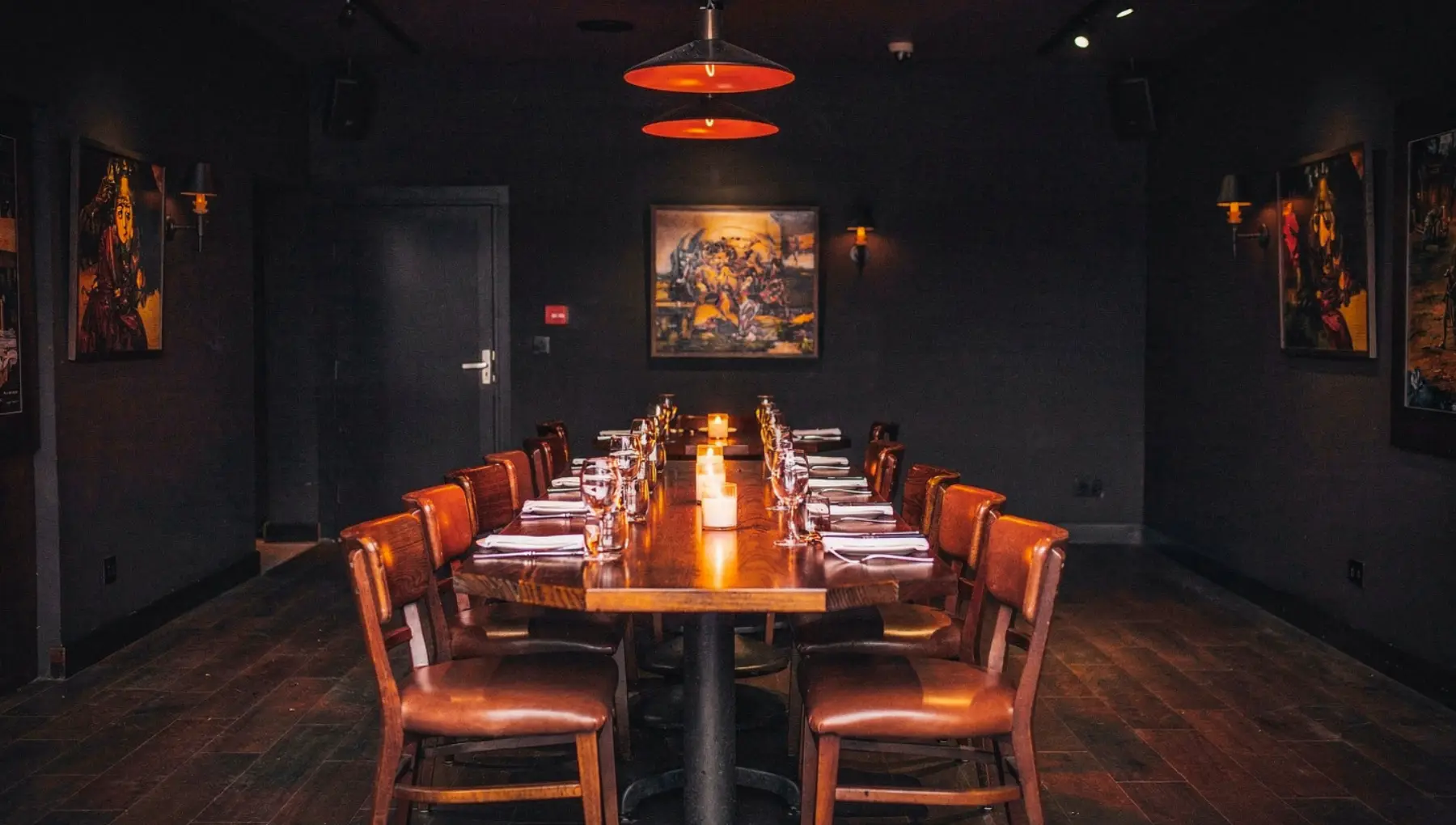 A large private dining room set for the evening, a long candlelit table and leather booths.